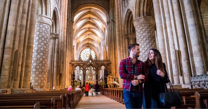man and woman linking arms, smiling at each other walking down main Nave of Durham Cathedral